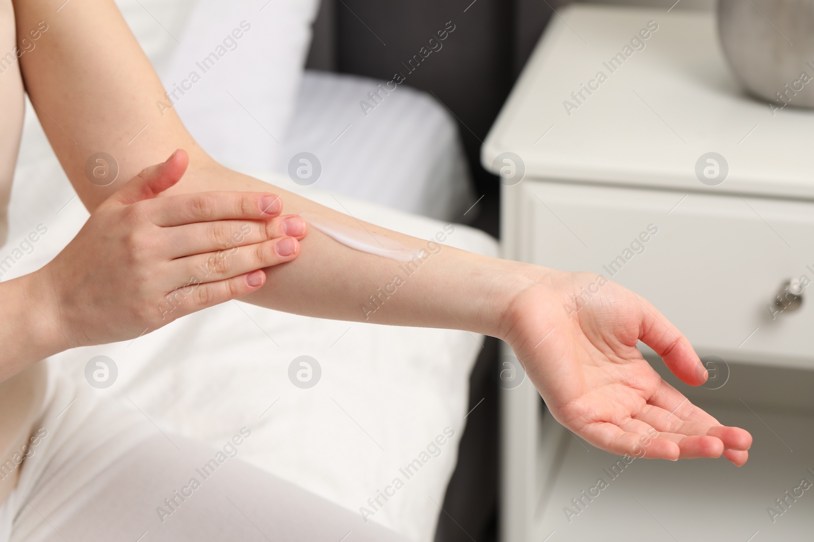 Photo of Young woman with dry skin applying cream onto her arm indoors, closeup