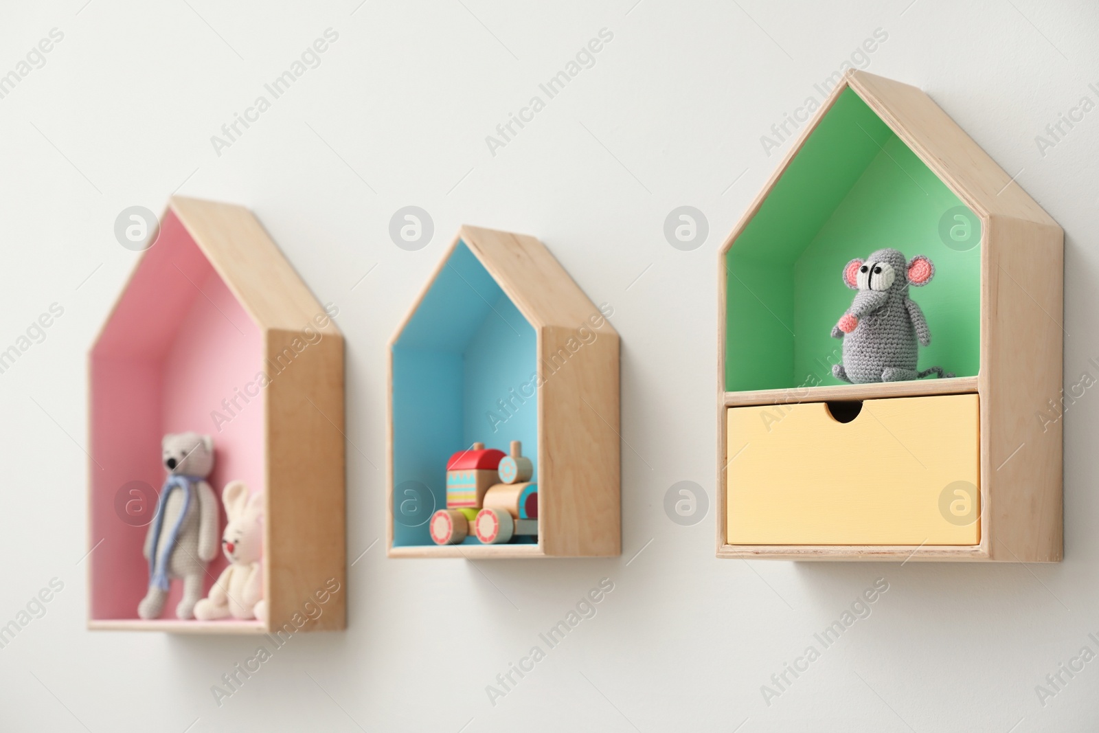 Photo of Stylish house shaped shelves with toys on white wall. Baby room interior design