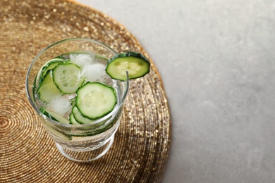 Photo of Glass of fresh cucumber water on golden mat. Space for text