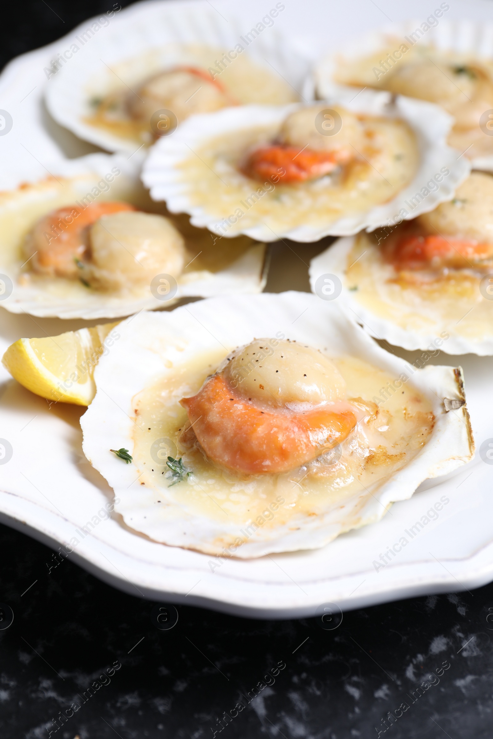 Photo of Fried scallops in shells and lemon on black table, closeup