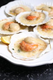 Fried scallops in shells and lemon on black table, closeup