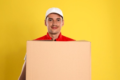 Photo of Happy young courier with cardboard box on yellow background
