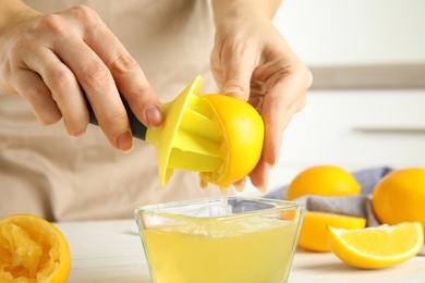 Photo of Woman squeezing lemon juice with reamer at table, closeup
