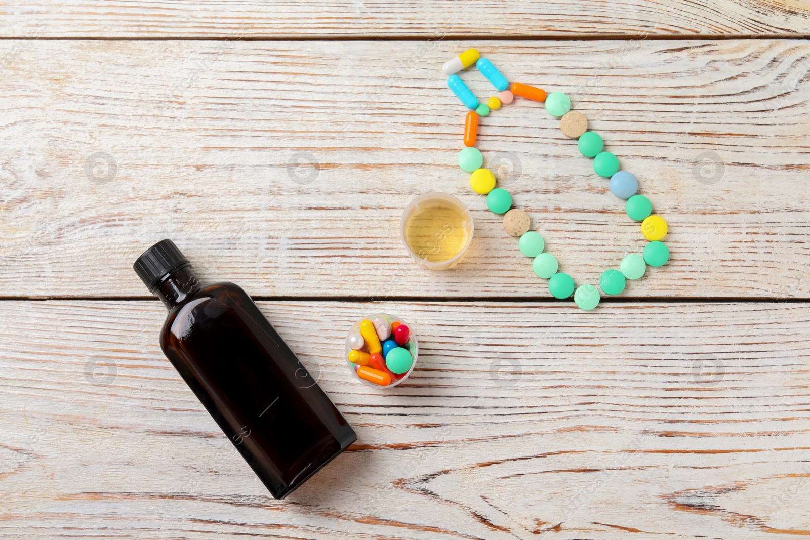 Photo of Flat lay composition with bottle of syrup, measuring cups and pills on white wooden table. Cold medicine