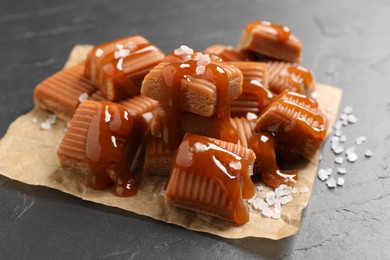 Tasty caramel candies with sauce and sea salt on grey table, closeup