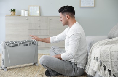 Photo of Man sitting on floor near electric heater at home