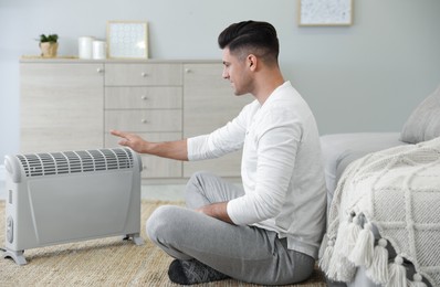 Man sitting on floor near electric heater at home