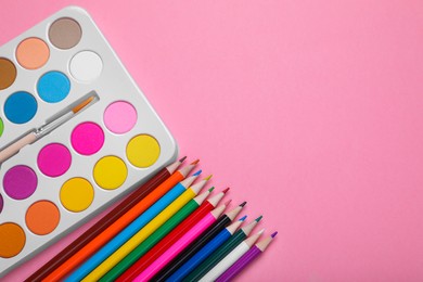 Photo of Watercolor palette with brush and colorful pencils on pink background, flat lay. Space for text