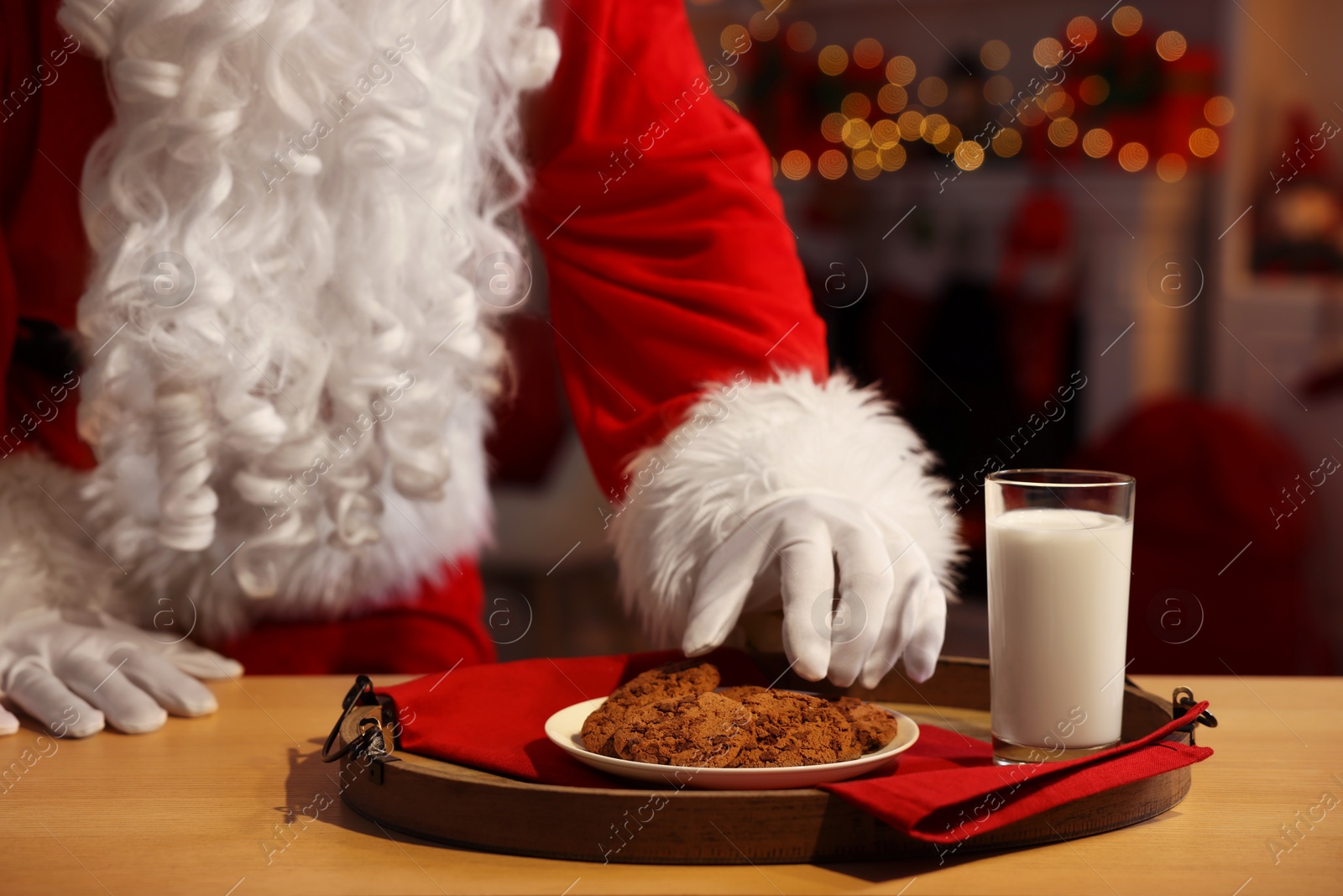 Photo of Merry Christmas. Santa Claus taking cookies from plate on table in room, closeup