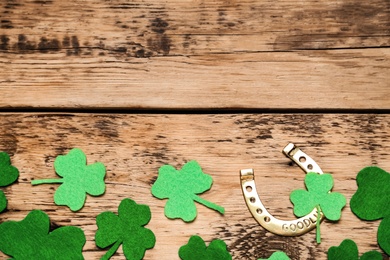 Photo of Golden horseshoe and decorative clover leaves on wooden table, flat lay with space for text. Saint Patrick's Day celebration