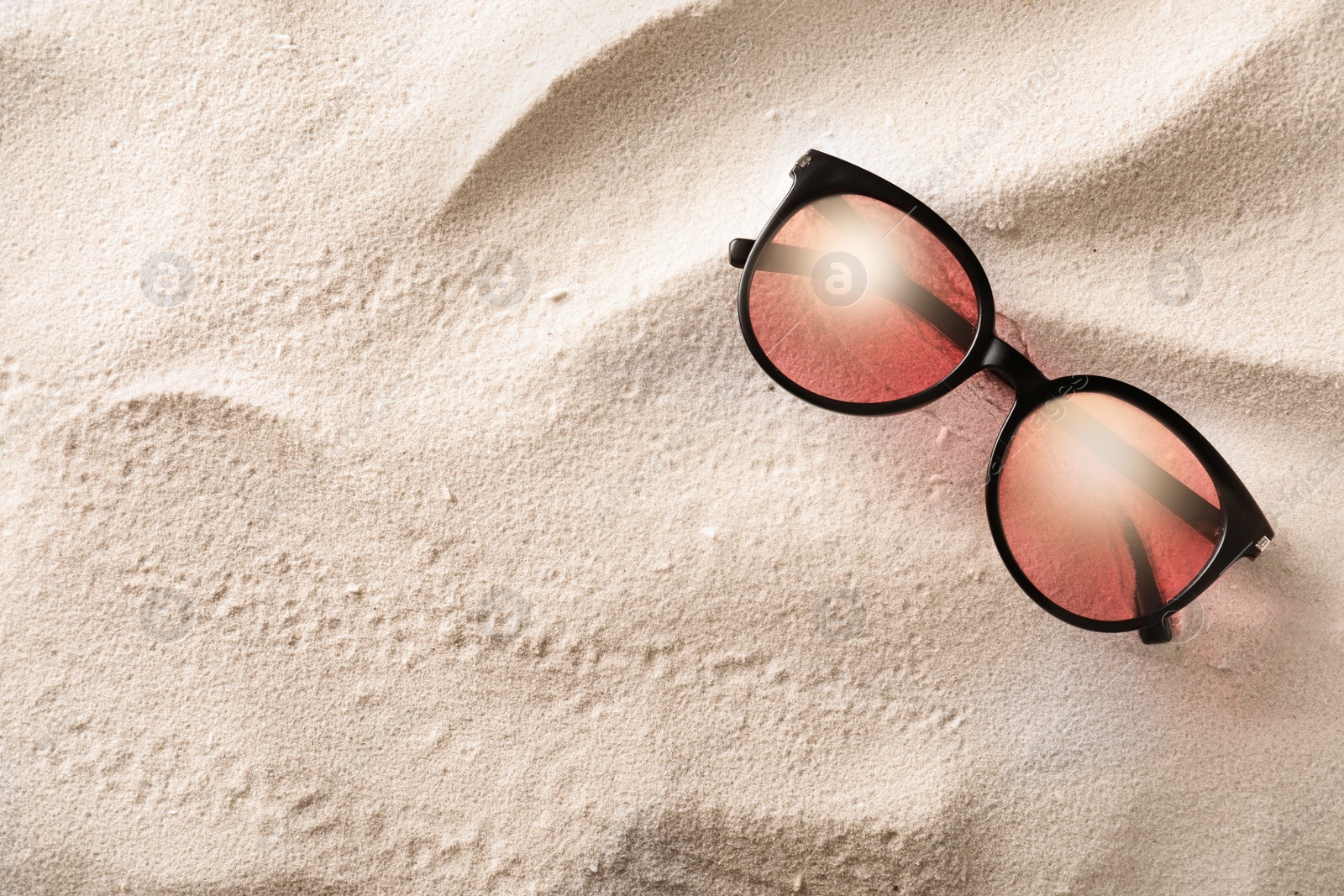 Photo of Stylish sunglasses on white sand, top view. Space for text