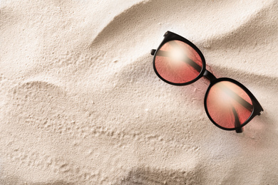 Stylish sunglasses on white sand, top view. Space for text