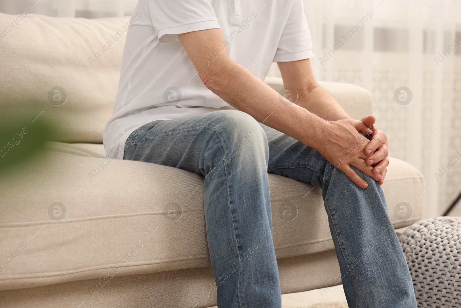 Photo of Senior man suffering from pain in knee at home, closeup. Rheumatism symptom