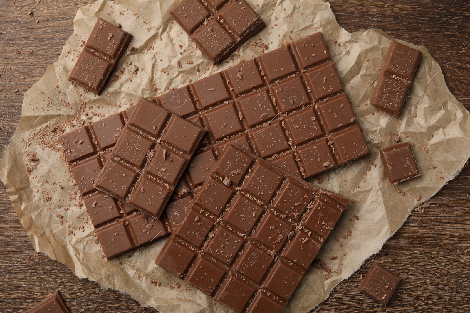 Photo of Pieces and crumbs of tasty chocolate bars on wooden table, flat lay