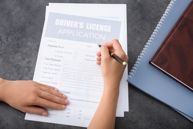 Man filling in driver's license application form at grey table, top view