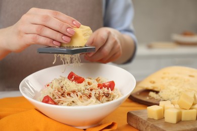 Photo of Woman grating cheese onto delicious pasta at table in kitchen, closeup