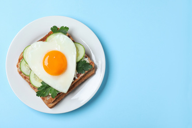 Photo of Plate of tasty sandwich with heart shaped fried egg on light blue background, top view. Space for text