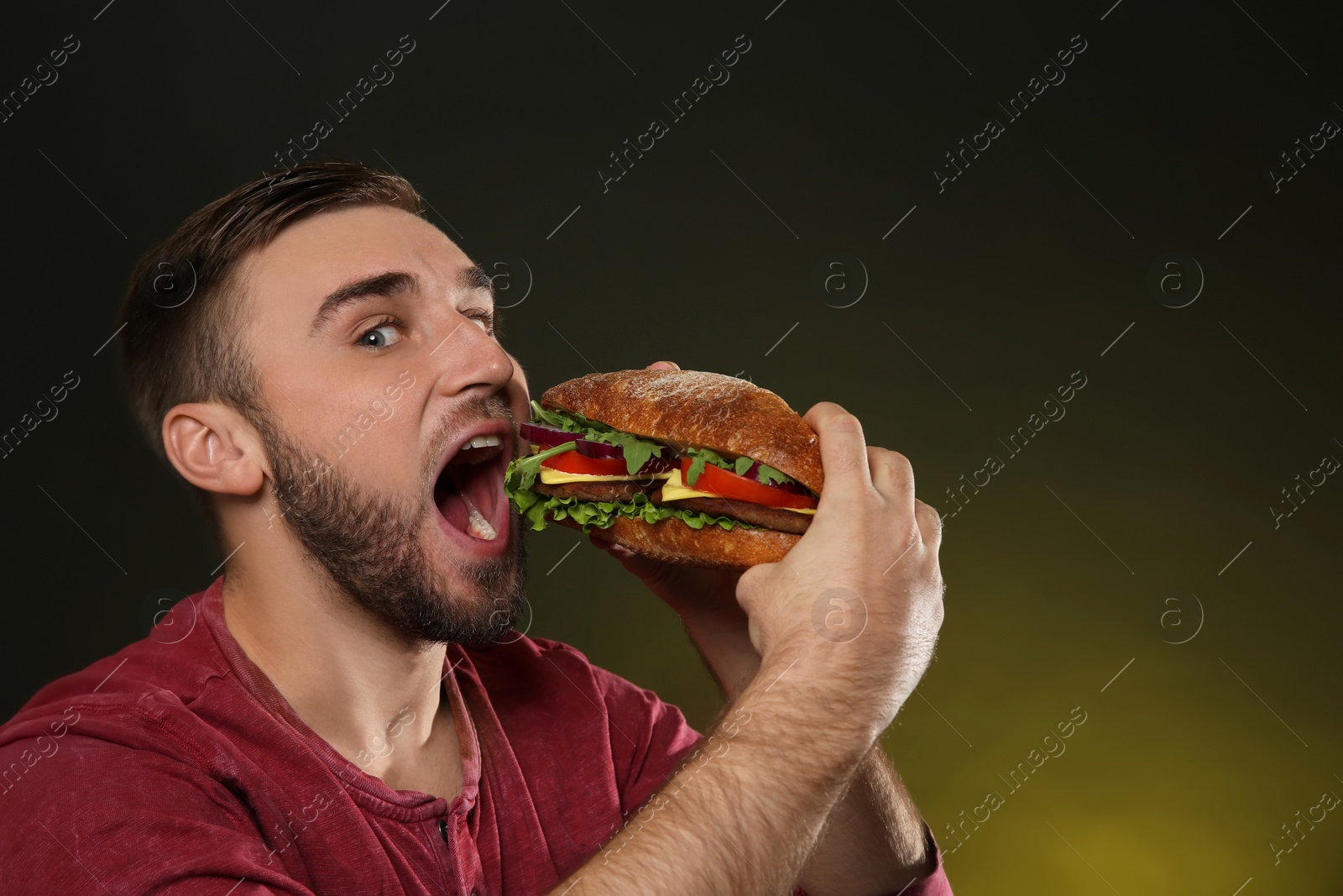 Photo of Young man eating tasty burger on color background. Space for text