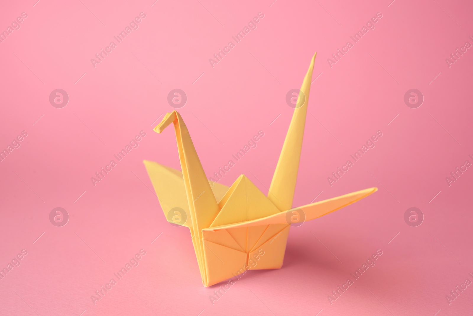 Photo of Origami art. Handmade paper crane on pink background