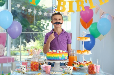 Photo of Happy boy near table with treats at birthday party indoors