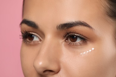 Photo of Woman with cream around eye on pink background, closeup. Skin care