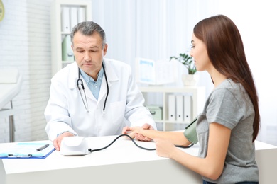 Photo of Young woman visiting doctor in hospital. Measuring blood pressure and checking pulse