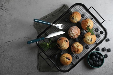Photo of Delicious muffins with powdered sugar, blueberries and cutlery on light grey table, flat lay