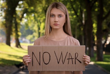 Photo of Sad woman holding poster with words No War in park