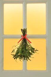 Photo of Mistletoe bunch with red bow hanging on window. Traditional Christmas decor