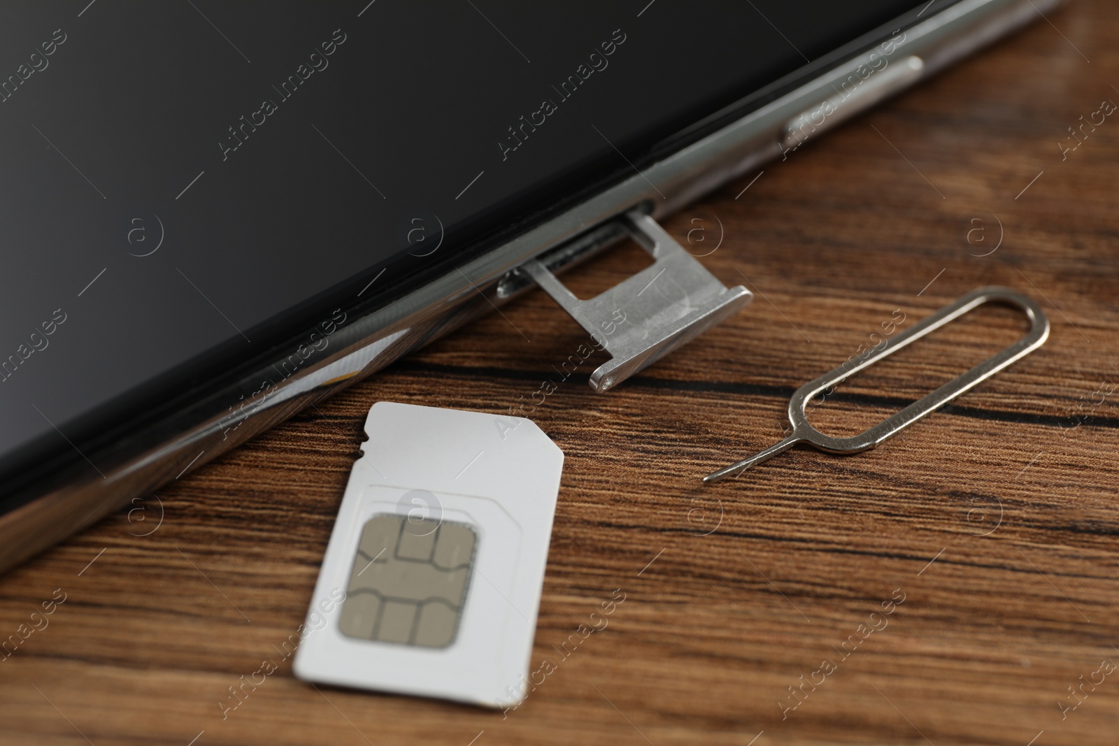 Photo of SIM card, mobile phone and ejector tool on wooden table, closeup