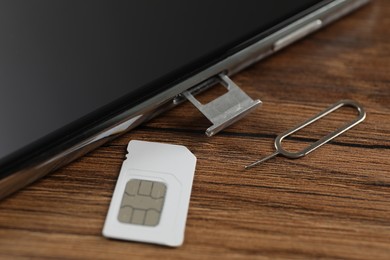 SIM card, mobile phone and ejector tool on wooden table, closeup