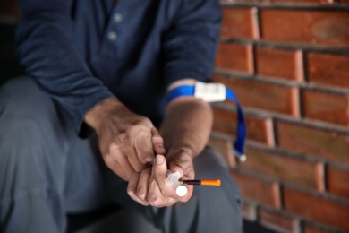 Photo of Male drug addict with syringe sitting near brick wall