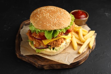 Photo of Delicious burger with crispy chicken patty, french fries and sauce on black table