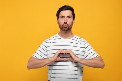 Handsome man making heart with hands and blowing kiss on orange background