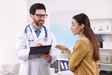 Photo of Doctor with clipboard consulting patient during appointment in clinic