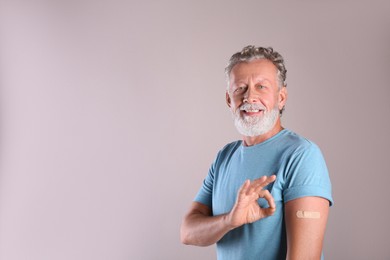 Photo of Cheerful senior man showing arm with bandage after vaccination on beige background. Space for text