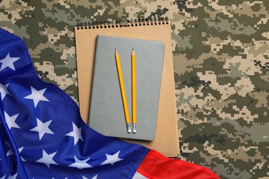 Photo of Notebooks, pencils and flag of United States on camouflage background, flat lay. Military education