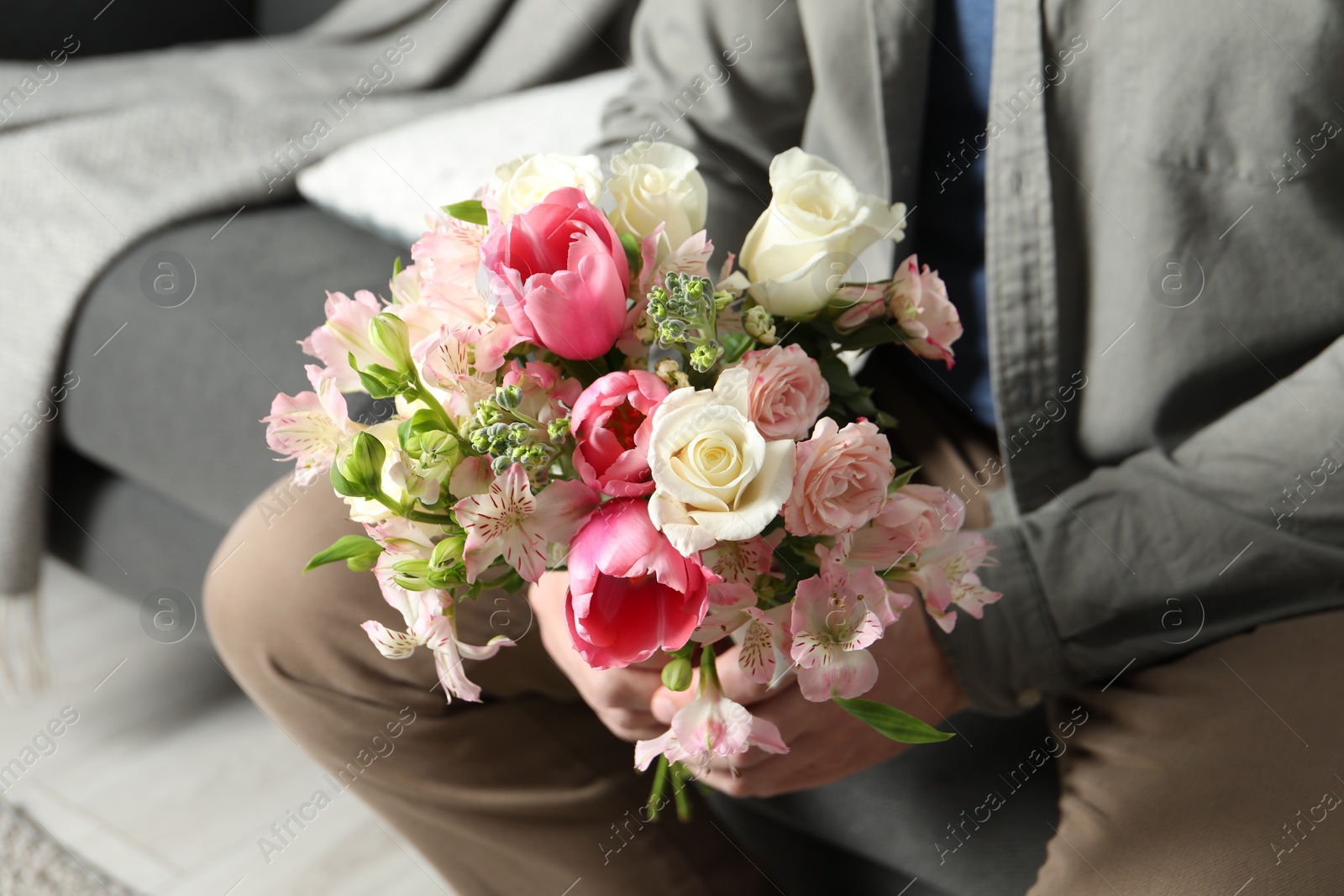 Photo of Man holding bouquet of beautiful flowers indoors, closeup