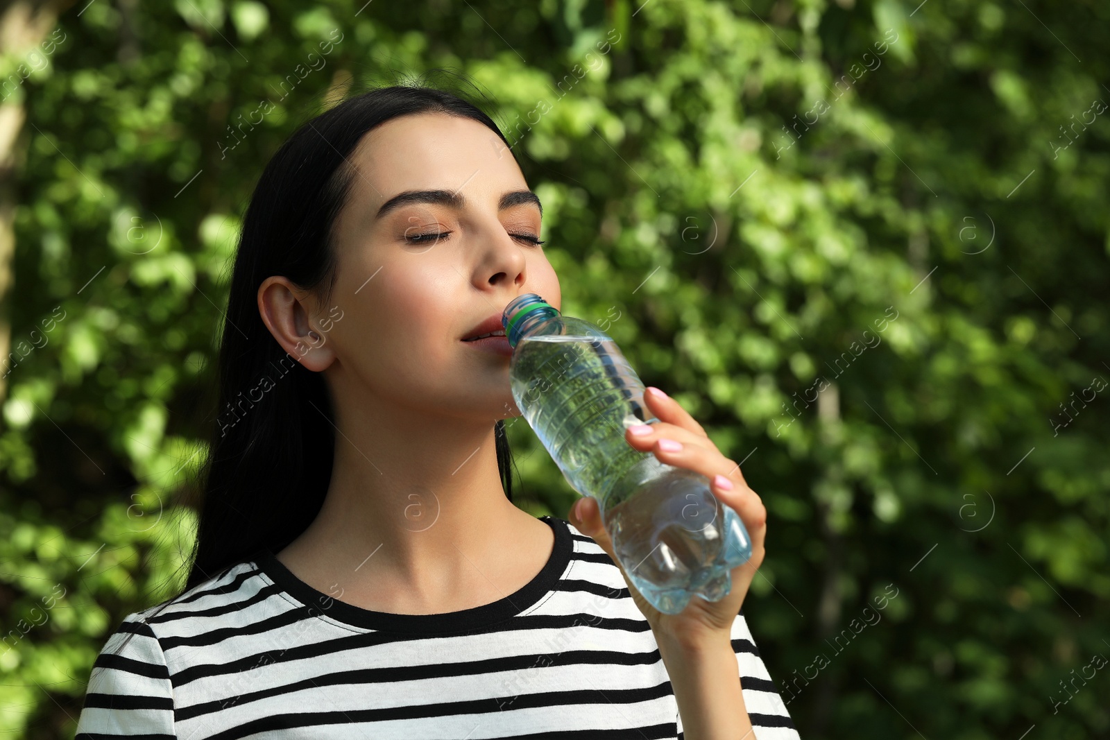 Photo of Beautiful young woman drinking water outdoors. Refreshing drink