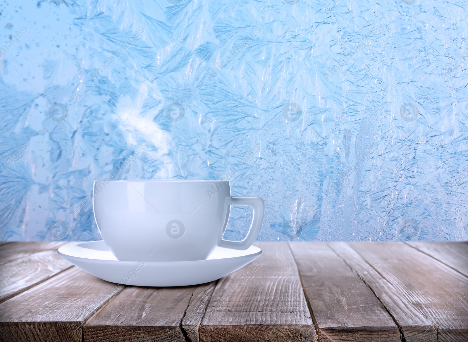 Image of Cup of hot tea on table near window covered with frost 