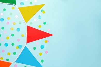 Bunting with colorful triangular flags and confetti on light blue background, flat lay. Space for text