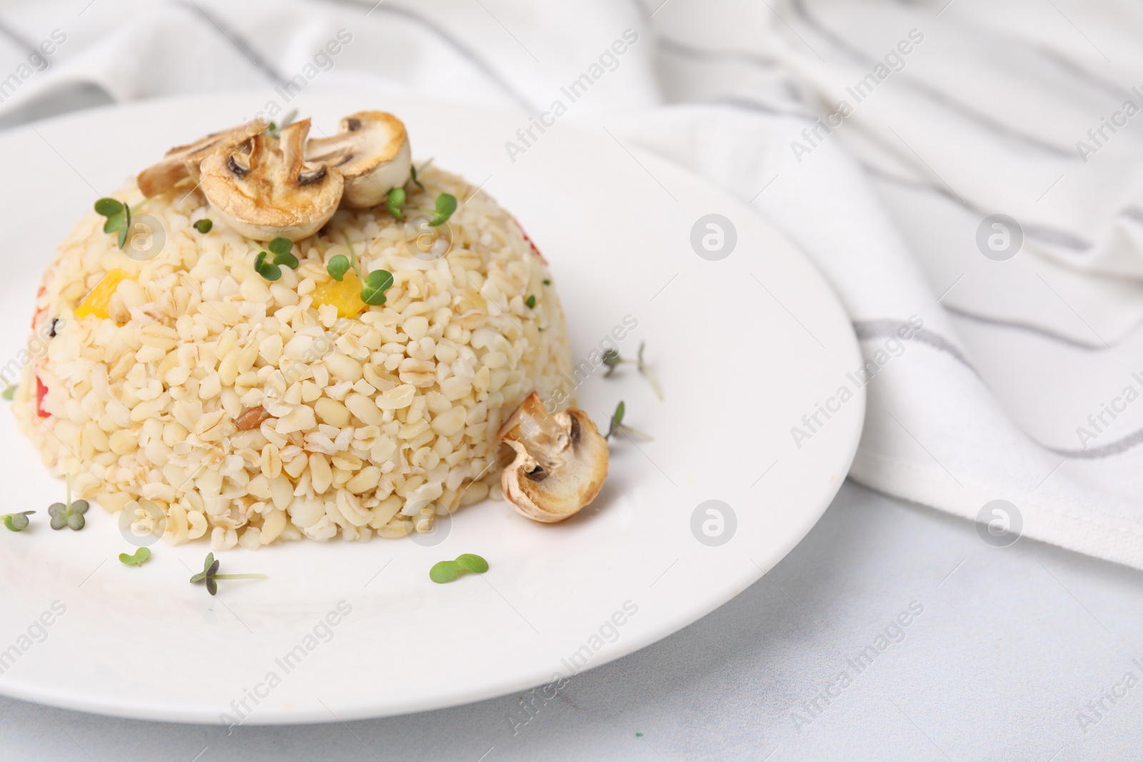 Photo of Delicious bulgur with vegetables, mushrooms and microgreens on table, closeup