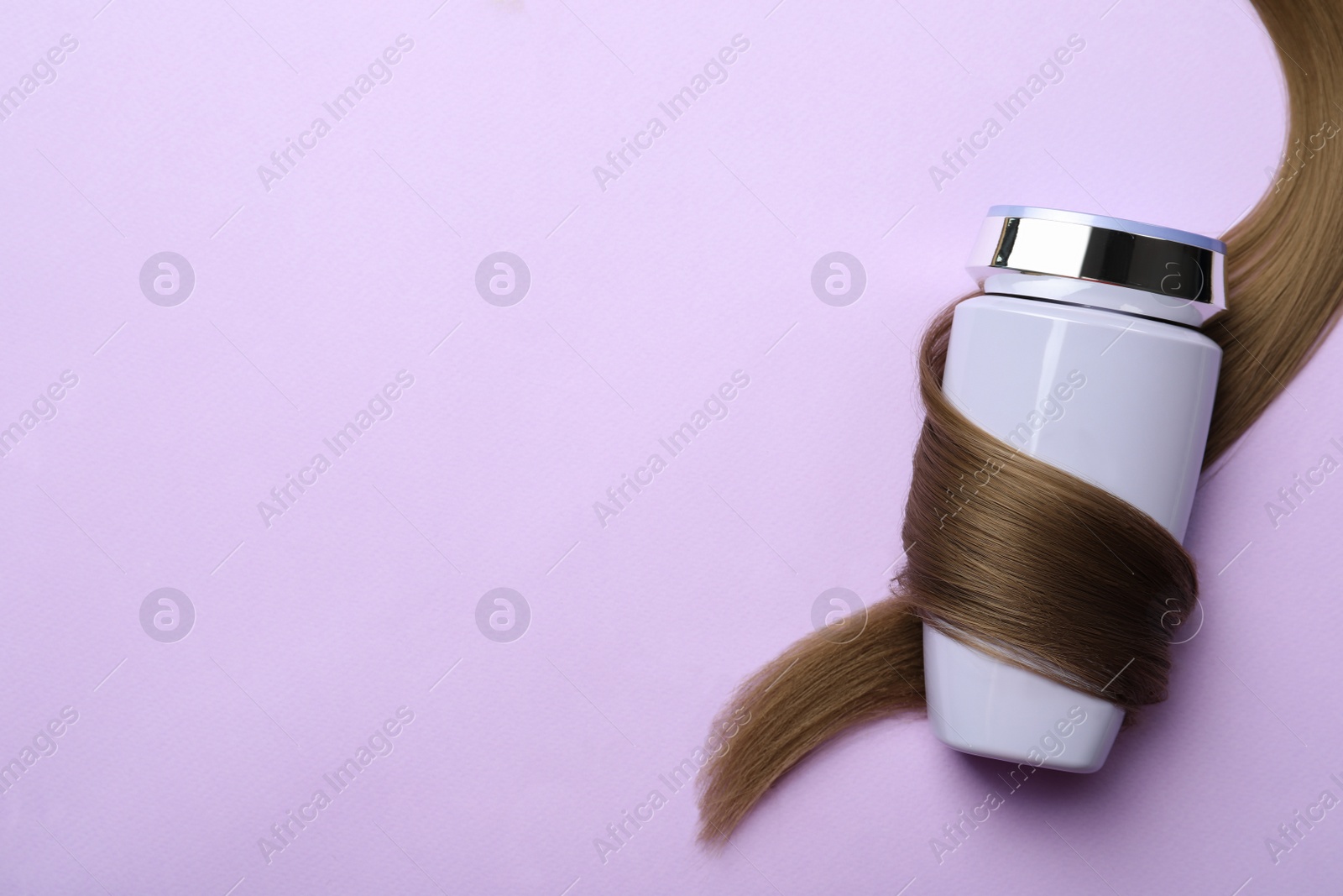 Photo of Bottle wrapped in lock of hair on violet background, top view with space for text. Natural cosmetic product
