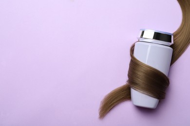 Bottle wrapped in lock of hair on violet background, top view with space for text. Natural cosmetic product