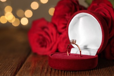 Photo of Beautiful engagement ring with gemstone in box and roses on wooden table
