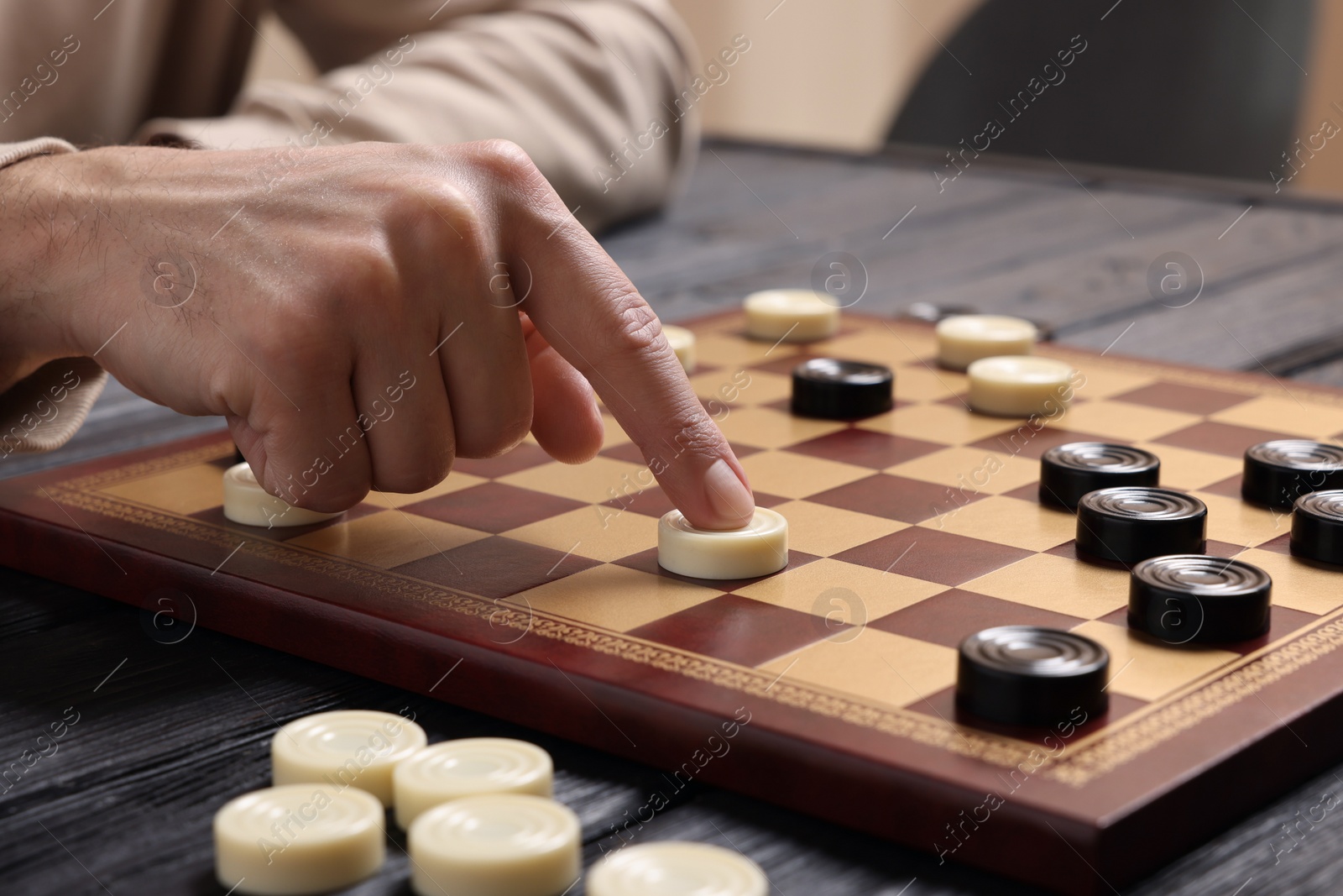 Photo of Playing checkers. Man thinking about next move at wooden table, closeup