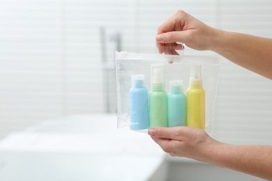 Photo of Woman with plastic bag of cosmetic travel kit in bathroom, closeup and space for text. Bath accessories