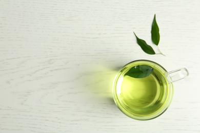 Cup of aromatic green tea and leaves on light wooden table, flat lay. Space for text