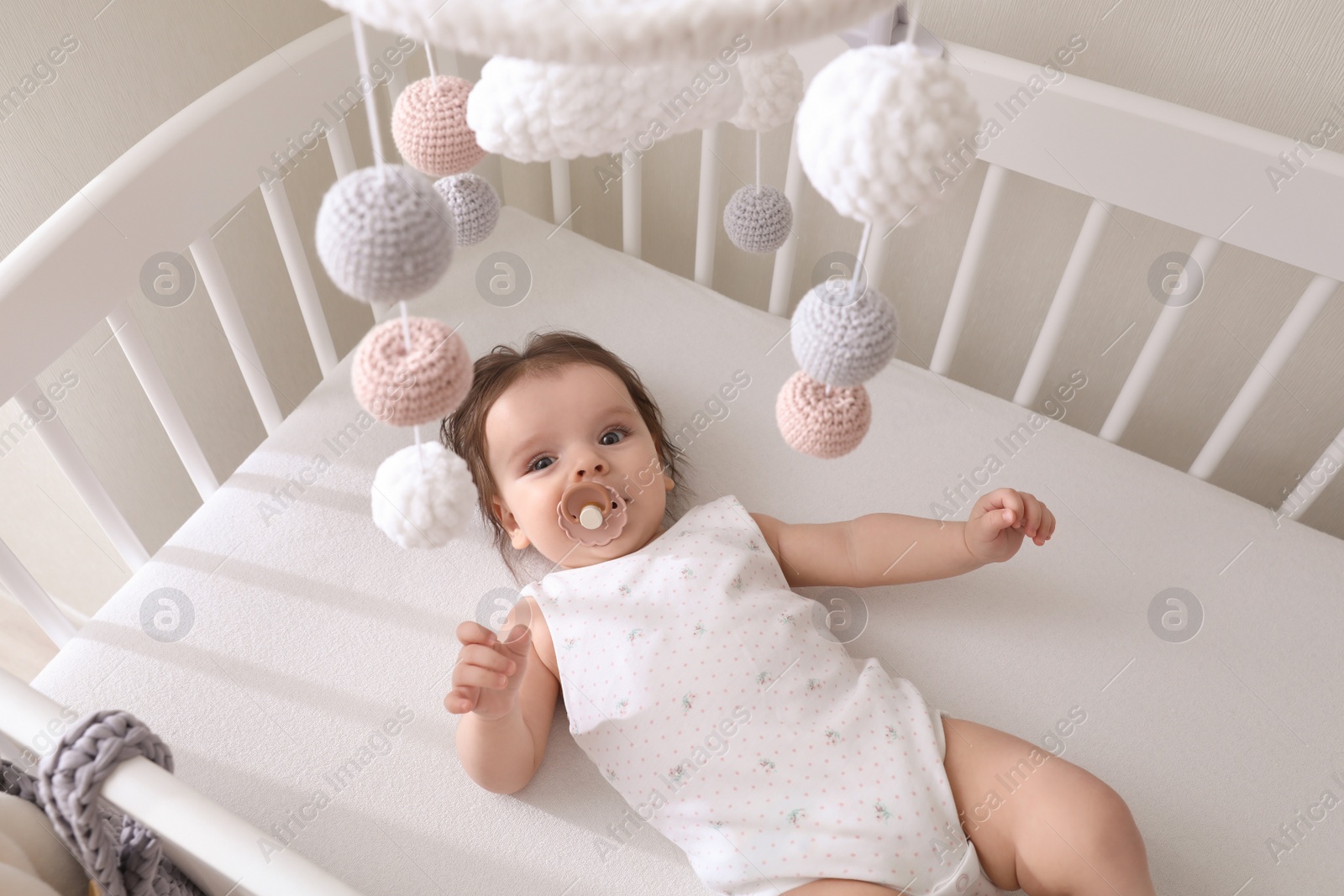 Photo of Cute little baby lying in crib with hanging mobile