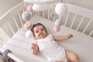 Photo of Cute little baby lying in crib with hanging mobile